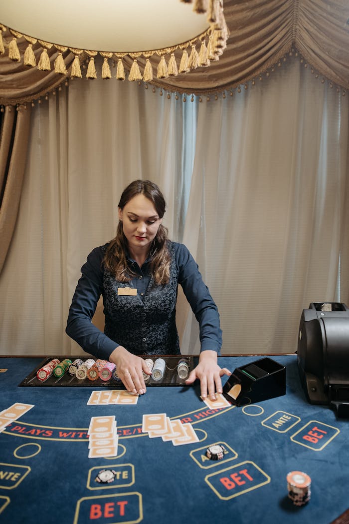 A female dealer managing chips and cards on a casino gaming table indoors.